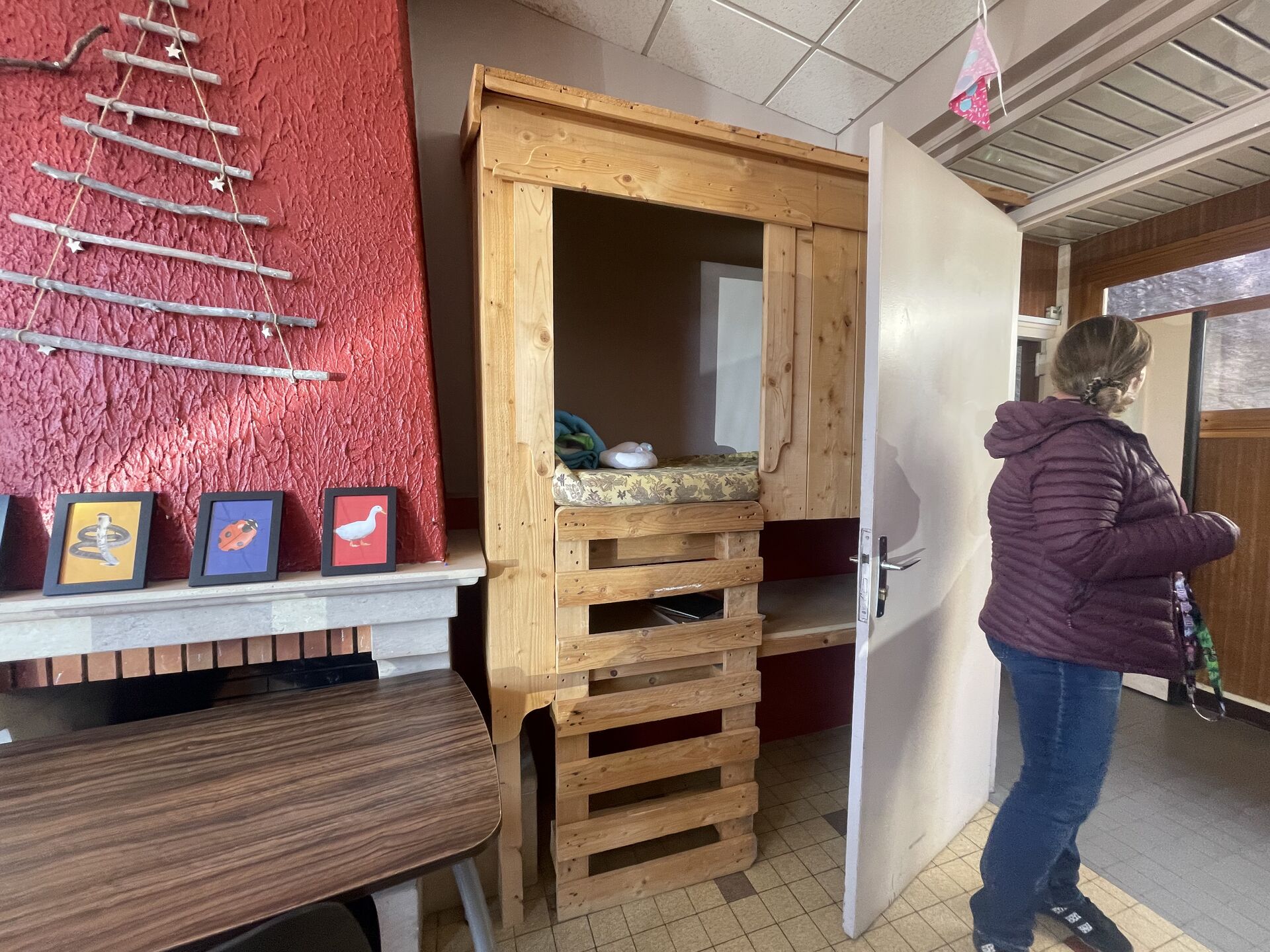 Coin cabane en bois aménagé, une éducatrice de dos ouvre une porte